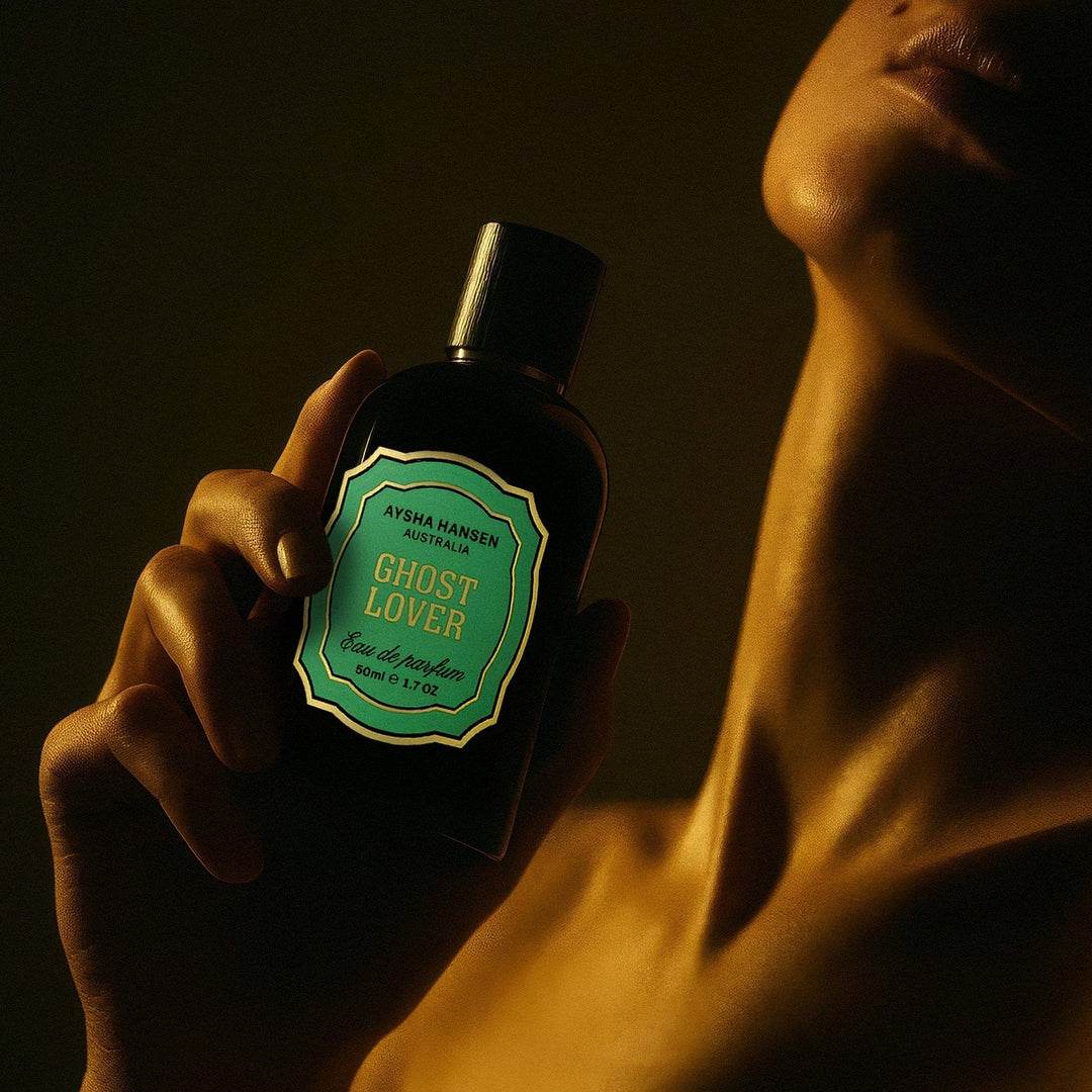 Person holding a bottle of Ghost Lover perfume against a dark background